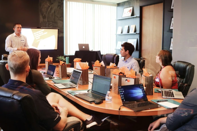 man standing in front of people sitting beside table, meeting with laptop computers